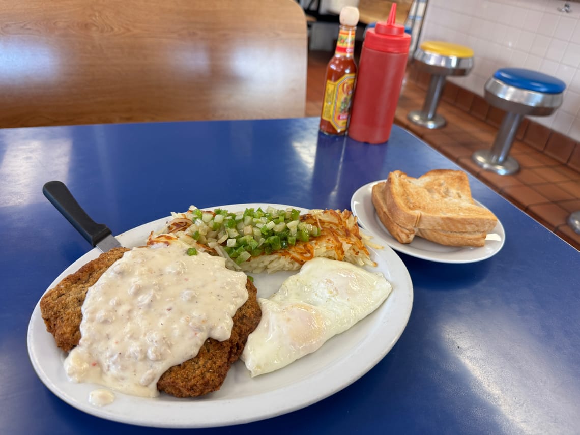 Country fried steak with sausage gravy, over easy eggs, hashbrowns topped with pepper and onions, and buttered toast. 